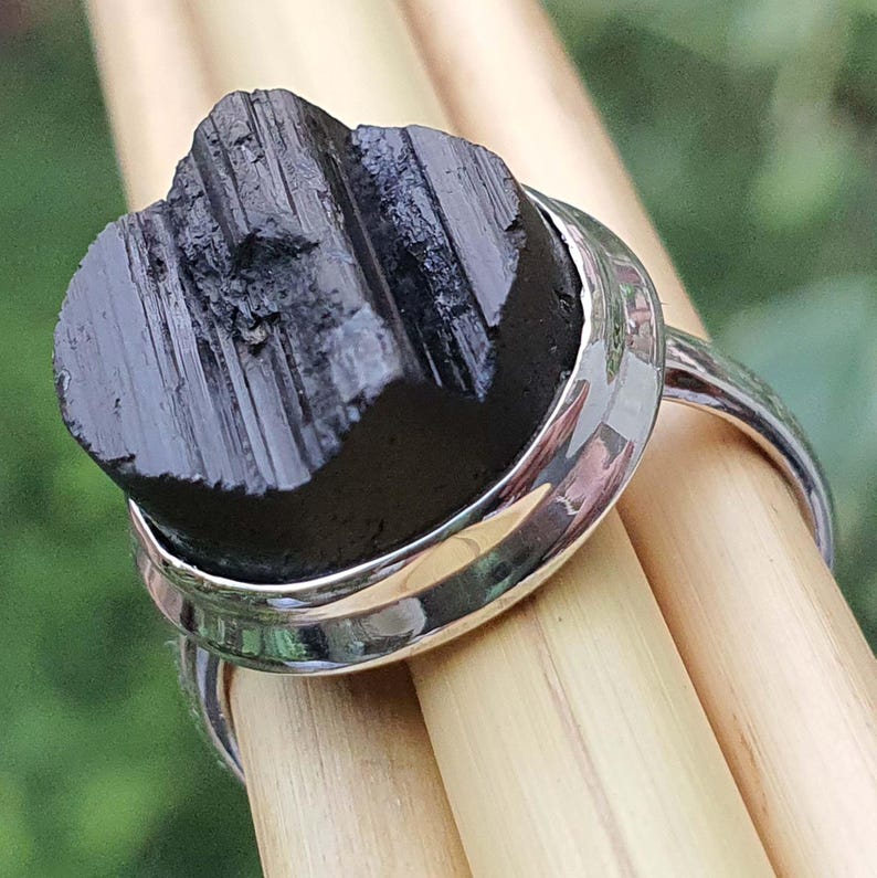 Op de afbeelding: Een zilveren ring met een zwarte, ruwe, natuurlijke steen in een bezel-setting. De steen heeft een gestreepte textuur.