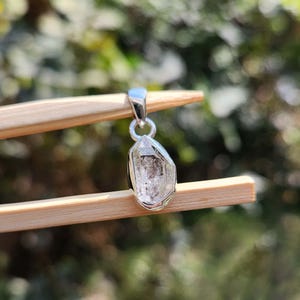 May include: A silver pendant featuring a clear, faceted, raw diamond crystal.