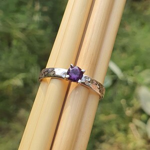 May include: A silver ring with a hammered texture and a round, purple gemstone set in the centre.