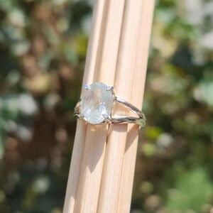 May include: A silver ring featuring a large, oval-shaped, translucent light blue gemstone held in a four-prong setting. The band of the ring has a textured, organic, branch-like appearance with a polished metallic finish.