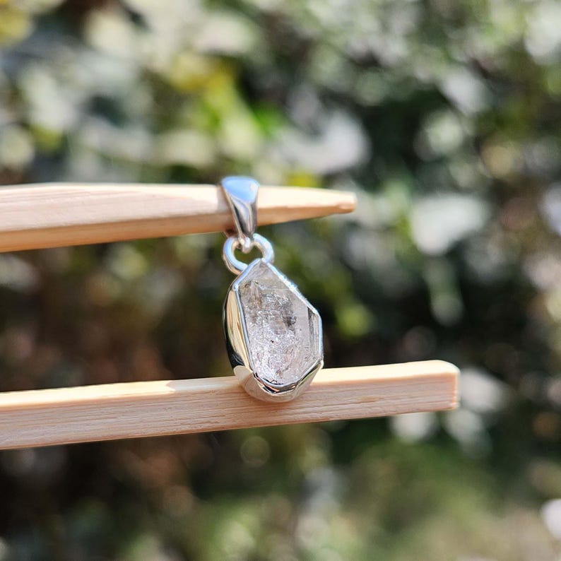 May include: A silver pendant featuring a clear, faceted, raw diamond crystal.
