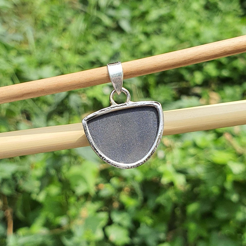 May include: A silver pendant with a half-circle shaped black stone. The pendant is hanging from a wooden stick.