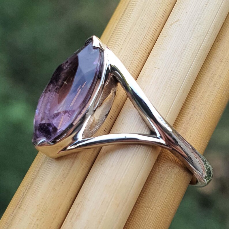 May include: A silver ring featuring a large, marquise-cut amethyst gemstone. The purple gemstone is set in a polished silver band, creating a striking contrast. The ring's design is simple yet elegant, suitable for everyday wear or special occasions.