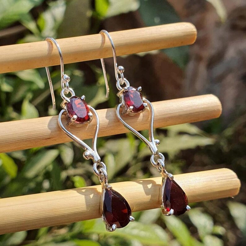 Puede incluir: Pendientes colgantes de plata con gemas rojas oscuras de forma ovalada y de l&aacute;grima. Los pendientes tienen un dise&ntilde;o calado delicado con cierre de gancho. Las gemas est&aacute;n engastadas en plata.