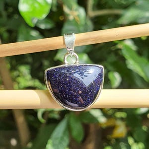 May include: A silver pendant with a blue, sparkly, semi-precious stone in a crescent shape.