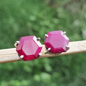 May include: A pair of silver stud earrings with red gemstone accents. The gemstones are faceted and have a hexagonal shape.