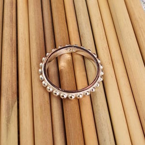 Op de afbeelding: Een zilveren ring met een kralenontwerp rond de band. De ring ligt op een lichtbruin houten oppervlak. De ring heeft een kleine inscriptie aan de binnenkant.