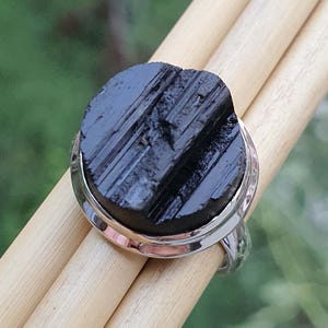 Op de afbeelding: Een zilveren ring met een zwarte, gestreepte, ovale edelsteen. De ring is gezet in een zilveren band met een gladde, gepolijste afwerking.