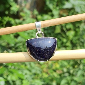 May include: A silver pendant with a dark blue, sparkly, semi-precious stone. The stone is cut in a half-moon shape and is set in a silver bezel.