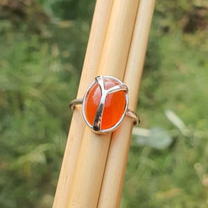 May include: A silver ring with an orange carnelian stone set in a peace sign design.