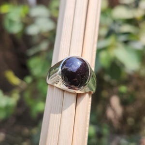 May include: A silver ring with a black gemstone. The gemstone has a round cabochon cut and is set in a bezel setting.