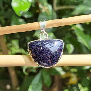 May include: A silver pendant with a blue, sparkly, semi-precious stone in a crescent shape.