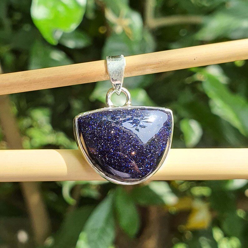 May include: A silver pendant with a blue, sparkly, semi-precious stone in a crescent shape.