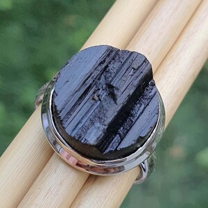 Op de afbeelding: Een zilveren ring met een zwarte toermalijn edelsteen. De edelsteen heeft een gestreept patroon en is gezet in een zilveren band.