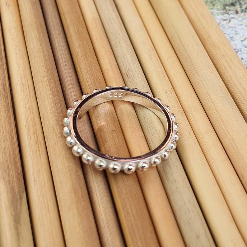 Op de afbeelding: Een zilveren ring met een kralenontwerp rond de band. De ring is gemaakt van glanzend metaal en is geplaatst tegen een houten achtergrond. De ring is maat 17 (NL).