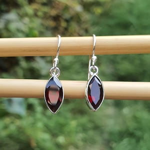 May include: A pair of silver dangle earrings with red gemstone marquise-shaped drops.
