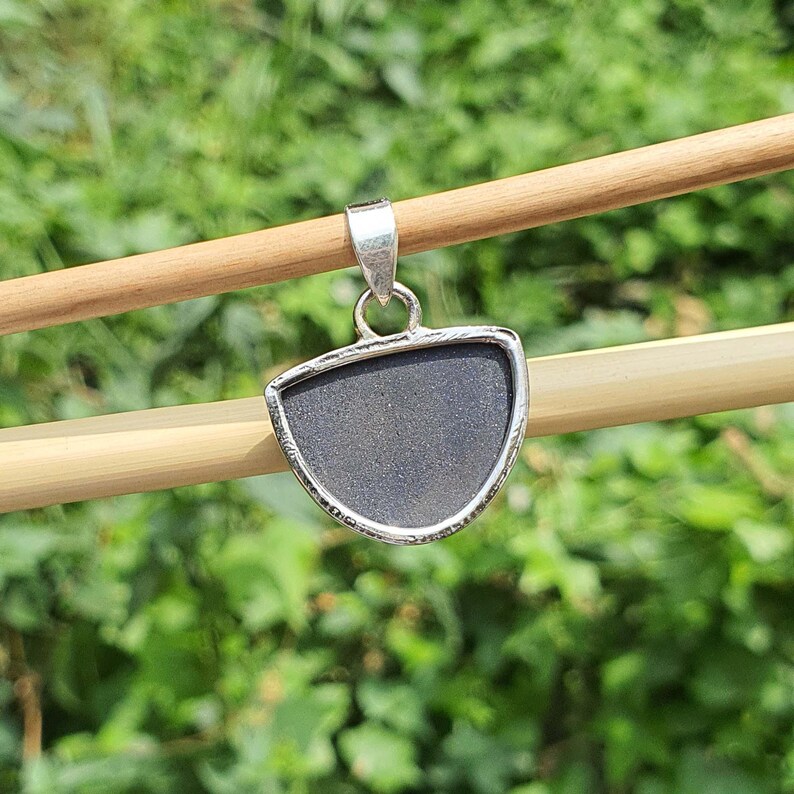 May include: A silver pendant with a half-circle shaped black stone. The pendant is hanging from a wooden stick.