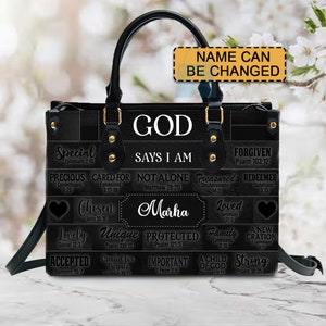 May include: Black leather handbag with gold accents and a design featuring the words "God Says I Am" and various bible verses. The name "Marha" is printed on the bag.