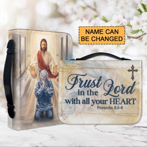 May include: A white and gold bible cover with a black handle. The cover features a painting of Jesus with a man kneeling in front of him. The text on the cover reads "Trust in the Lord with all your heart Proverbs 3:5-6".