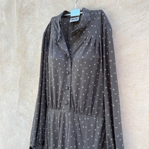 Könnte beinhalten: Ein langärmeliges graues Kleid mit weißem Blumenmuster. Das Kleid hat einen Knopfleisten vorne und eine geraffte Taille.