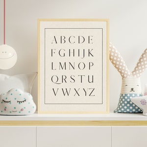 May include: A framed print with the alphabet in black letters on a white background. The print is on a shelf with a white cloud-shaped pillow and a stuffed bunny with polka dots.