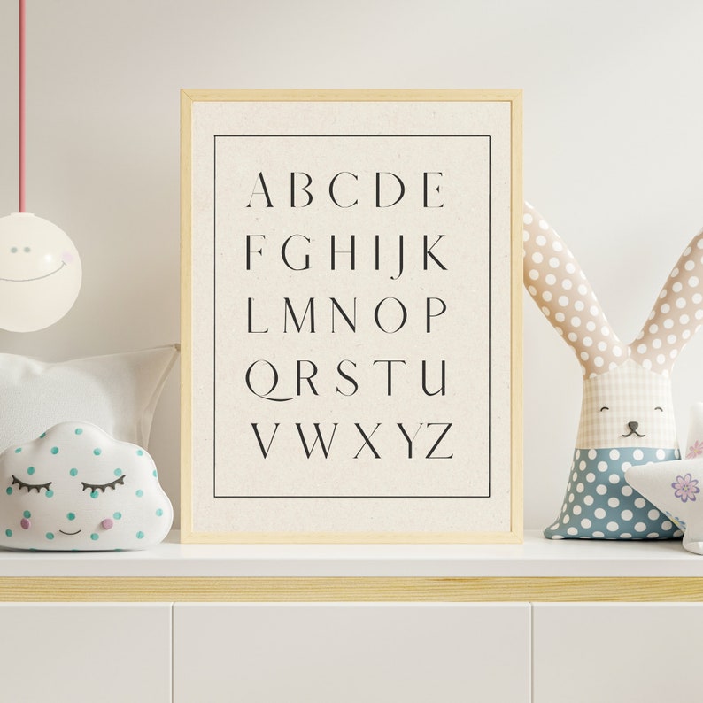 May include: A framed print with the alphabet in black letters on a white background. The print is on a shelf with a white cloud-shaped pillow and a stuffed bunny with polka dots.