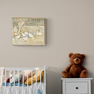 May include: A framed watercolor painting of a group of white geese in a pond with a tree in the background. The painting is hanging on a light beige wall above a white crib with a white and blue blanket and a brown teddy bear sitting on a white nightstand.