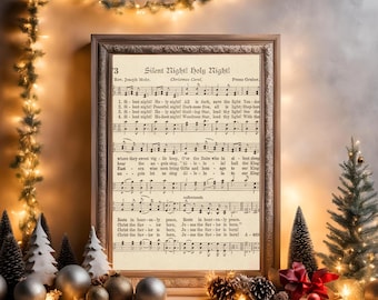 May include: A framed print of the Christmas carol "Silent Night! Holy Night!" with musical notes and lyrics. The print is in a wooden frame and is surrounded by Christmas decorations, including ornaments, small trees, and lights. The overall theme is festive.