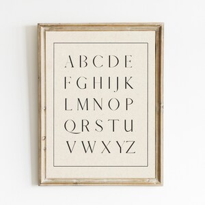 May include: A framed print of the alphabet in a simple, modern font. The letters are printed in black on a cream-colored background.