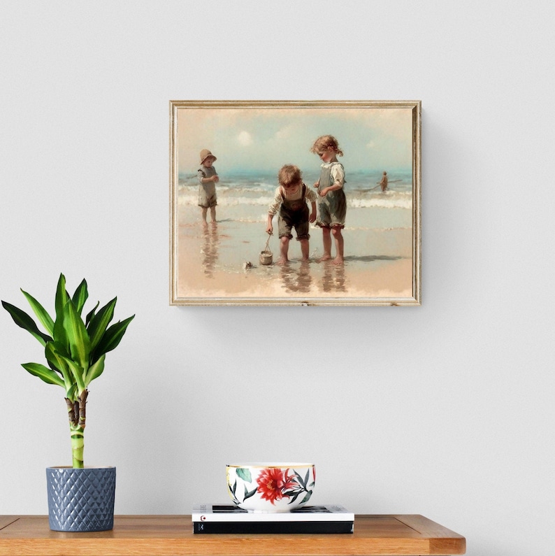 May include: A painting of three children playing on a beach. The children are wearing casual clothing and are playing with a bucket and shovel. The beach is sandy and the water is blue. The painting is framed in a light wood frame.