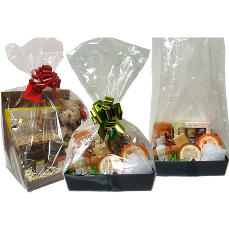 May include: Three gift baskets wrapped in clear cellophane with red, green, and gold bows. The baskets contain various items, including a teddy bear, bath products, and snacks.