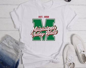 May include: White t-shirt featuring a green and red Mississippi Valley State logo. The logo displays a large "M" with the words "Mississippi Valley State" in a red cursive font. The text "EST. 1950" is positioned above the logo.