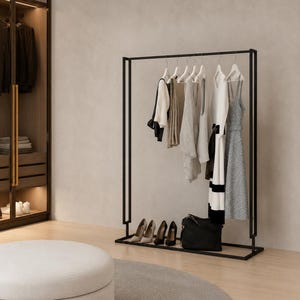 Puede incluir: Un perchero de metal negro con marco rectangular que sostiene varias prendas en perchas blancas, incluyendo un top blanco, camisas beige y grises, un vestido blanco con rayas negras y un vestido azul estampado, con zapatos y un bolso negro debajo.