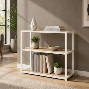 May include: A three-tiered bookshelf with a white metal frame and wooden shelves. The top shelf features a white geometric vase and books. The middle shelf has a small potted plant and a bowl. The bottom shelf displays books and a succulent.