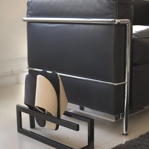 May include: A black leather sofa with chrome legs and a black metal shoe rack with two pairs of slippers underneath.