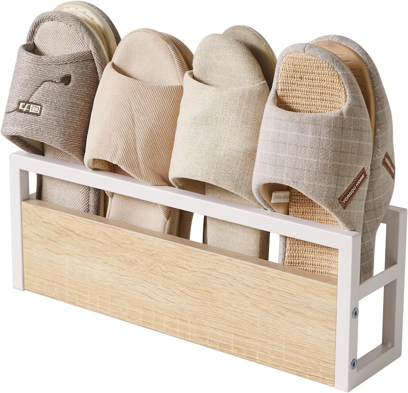 Puede incluir: Un zapatero de metal blanco y madera que contiene cuatro pares de zapatillas de tonos neutros. Las zapatillas var&iacute;an en textura y dise&ntilde;o, con algunos detalles bordados y materiales tejidos.