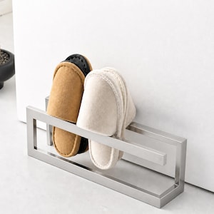 Matte silver metal wall mounted slipper holder with clean geometric structure. Minimalist shoe storage rack organizing indoor slippers. Modern wall mounted solution ideal for entryway, bathroom, or compact home spaces.