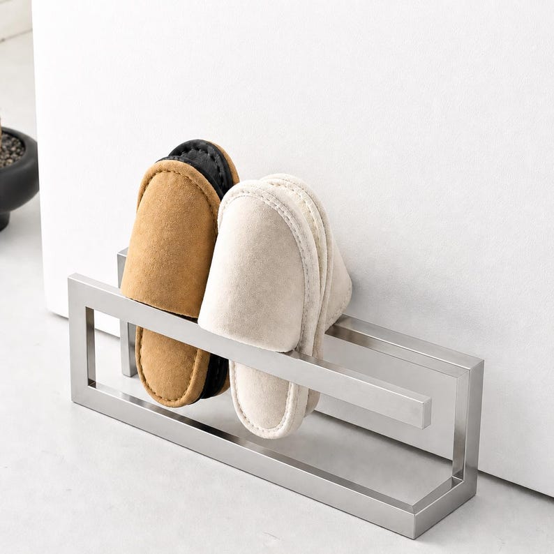 Matte silver metal wall mounted slipper holder with clean geometric structure. Minimalist shoe storage rack organizing indoor slippers. Modern wall mounted solution ideal for entryway, bathroom, or compact home spaces.
