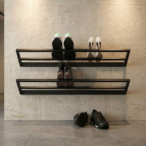 Puede incluir: Zapatero de metal negro con dos estantes, que muestra varios zapatos. El estante superior exhibe zapatillas deportivas y tacones, mientras que el estante inferior contiene botas. Un par de zapatillas y un zapato están en el suelo. El estante está montado en la pared.