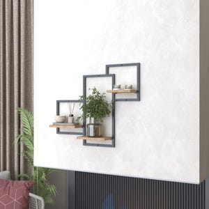 May include: Three black metal shelves with wooden shelves, mounted on a white wall. The top shelf has two small candles, the middle shelf has a small plant in a glass vase, and the bottom shelf has a small bowl and two bottles of essential oils.