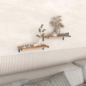 May include: Two wooden floating shelves with black metal brackets are mounted on a textured wall. The shelves display decorative vases, candles, and dried flowers, creating a minimalist aesthetic. The shelves are above a neutral-toned sofa.