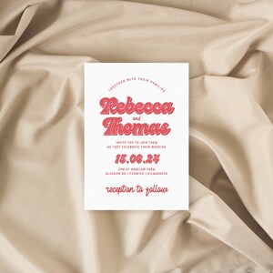 May include: A white wedding invitation with red text. The invitation reads "Rebecca and Thomas" in a retro font. The date of the wedding is listed as "15.06.24" and the location is "SPM at Marelam Farm, Glasgow Rd | Fenwick | Kilmarnock". The invitation concludes with "reception to follow".