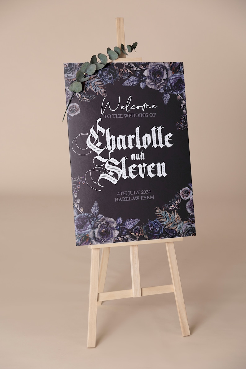 May include: A black welcome sign with white gothic lettering announcing the wedding of Charlotte and Steven. The sign is decorated with dark purple and blue floral illustrations and the date "4th July 2024" and the location "Harelaw Farm". The sign is displayed on a wooden easel.