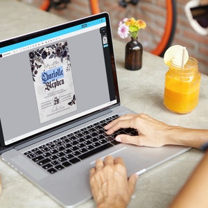 May include: A person using a laptop to edit a wedding invitation template. The invitation features a dark floral design with the text "Charlotte and Stephen" and a date of "Saturday, 28th of October".