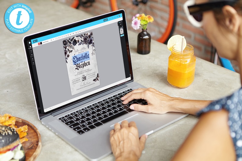 May include: A person using a laptop to edit a wedding invitation template. The invitation features a dark floral design with the text "Charlotte and Stephen" and a date of "Saturday, 28th of October".