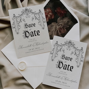 Op de afbeelding: Elegante trouwkaarten "Save the Date" met sierlijke zwart-witte ontwerpen. De kaarten tonen de tekst "Save the Date" en de namen Annabelle & Christopher, met de datum 28.05.2026. De enveloppen hebben een bloemeninterieur.