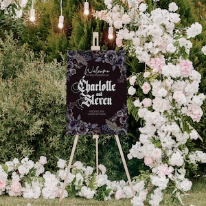 May include: A black wedding welcome sign with a dark floral design and the text "Welcome to the wedding of Charlotte and Steven 4th July 2024 Harklaw Farm".