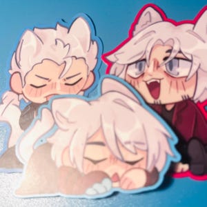 May include: Three stickers featuring anime-style characters with white hair and cat ears. The characters have various expressions, including sleeping and smiling. Each sticker has a blue or red outline.