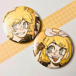 May include: Two yellow and white anime character buttons with a yellow background. The characters are holding a cassette tape and a microphone. The buttons are 5.7 cm in diameter.