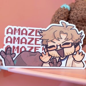 May include: A rectangular sticker featuring a cartoon character with light brown hair, glasses, and a wide smile, waving both hands. The text "AMAZE" is repeated three times in a red pixelated font. A large, dark brown rock shape is visible.